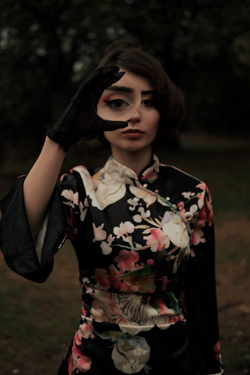 A Woman in Black Floral Dress Holding a Magnifying Glass
