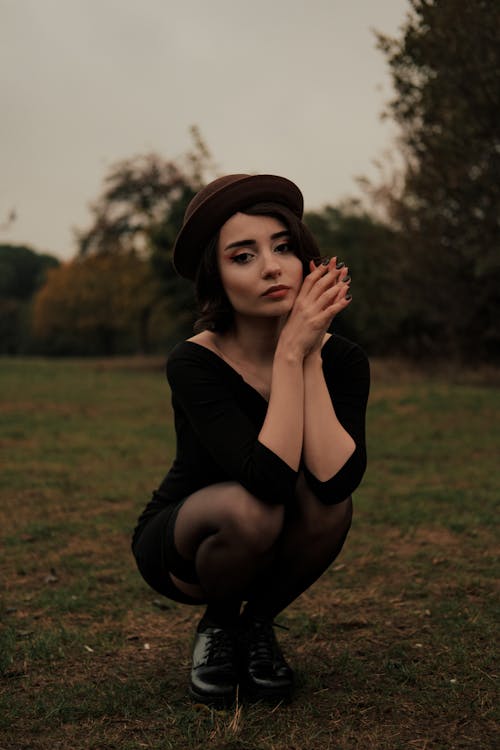 A Woman in Black Clothing Squatting on Grass