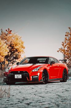 A vibrant red sports car parked on a road with autumn trees in the background.