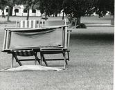 Monochrome image of empty deck chairs on grass in a park setting.