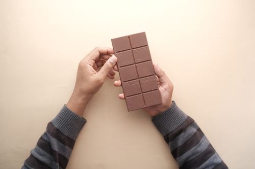 Free Close-up of hands holding a chocolate bar with a striped sweater, captured in natural light. Stock Photo