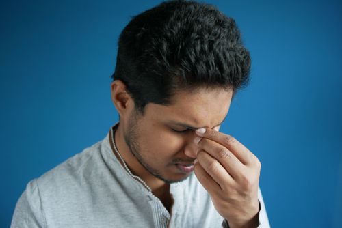 Free A man showing stress or headache by pinching his nose bridge against a blue backdrop. Stock Photo