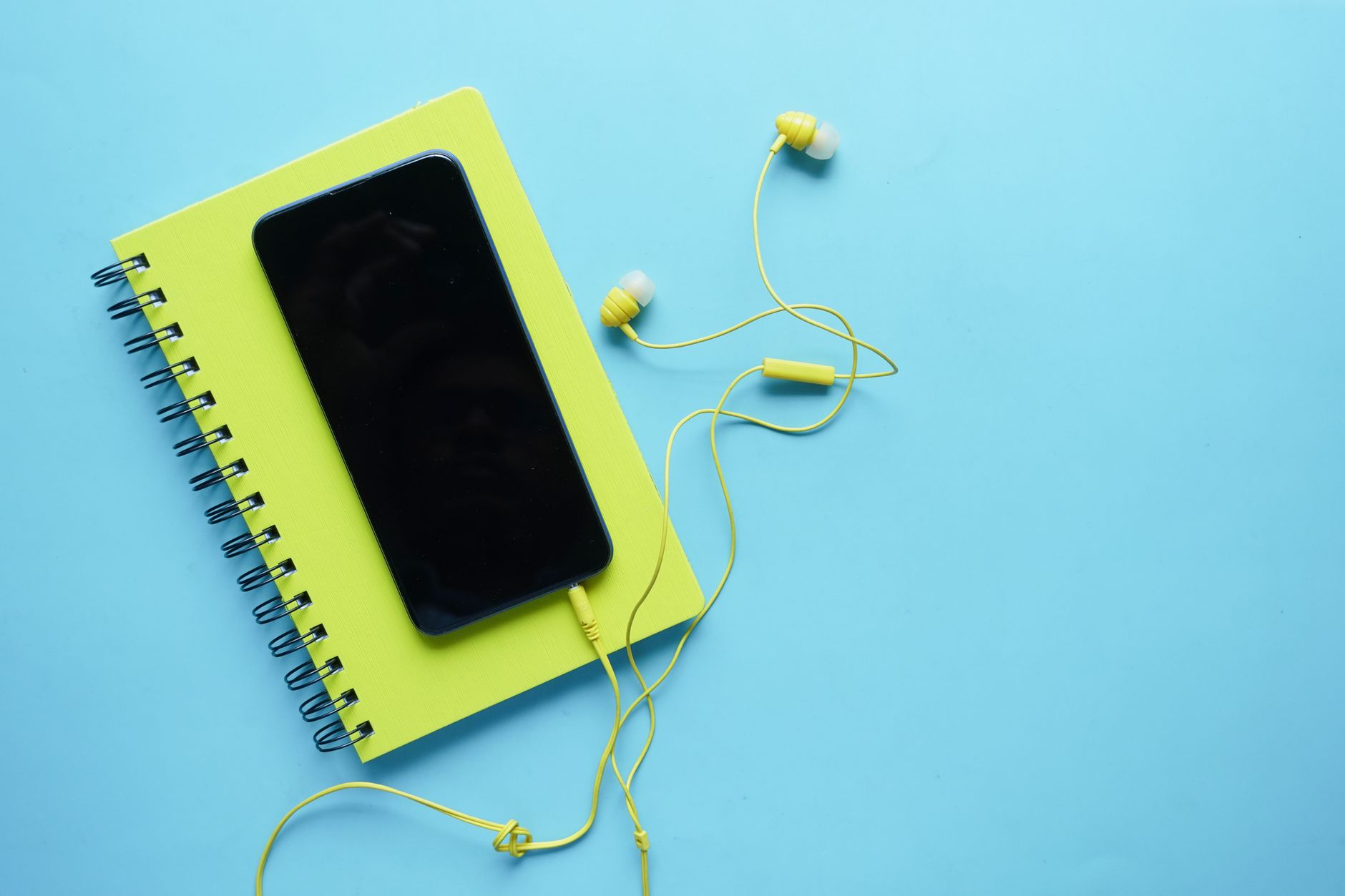 Colorful flat lay of a smartphone, notebook, and earbuds on a blue background. Perfect for tech and lifestyle themes.