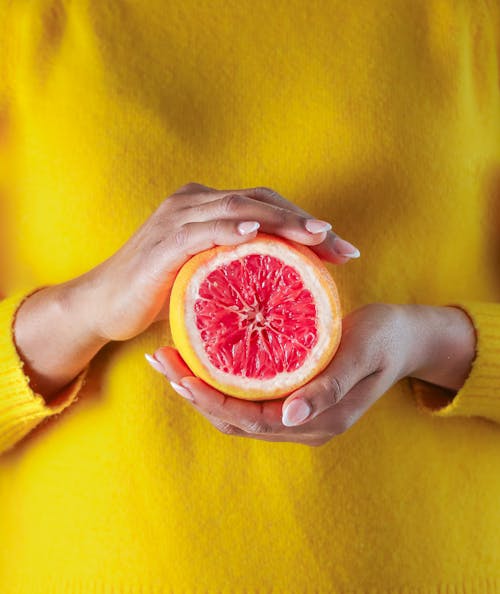 Free Woman in Yellow Sweater Holding a Cut Grapefruit Stock Photo