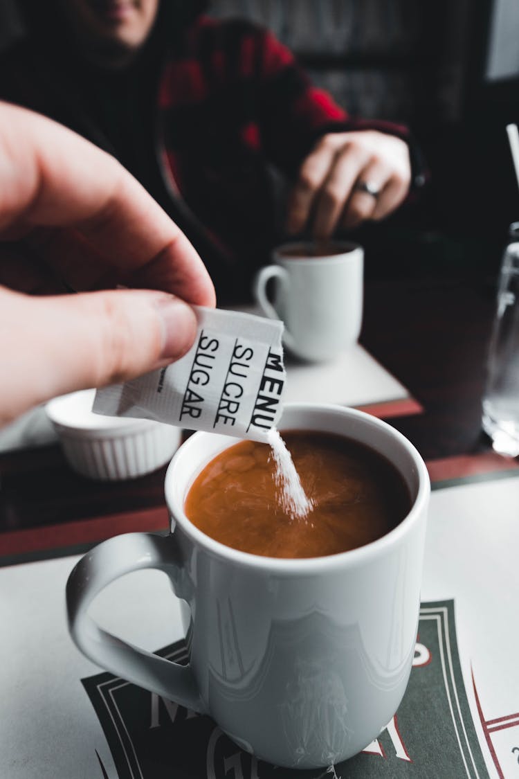 Person Putting Sugar Packet On Coffee