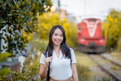 Free Asian woman smiling with a train in the background in vibrant Ho Chi Minh City setting. Stock Photo