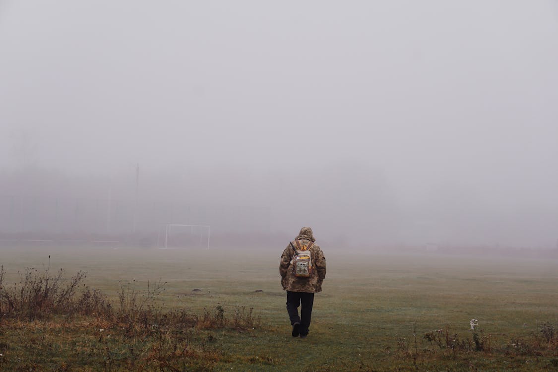 A Person in a Hoodie Walking on a Foggy Field