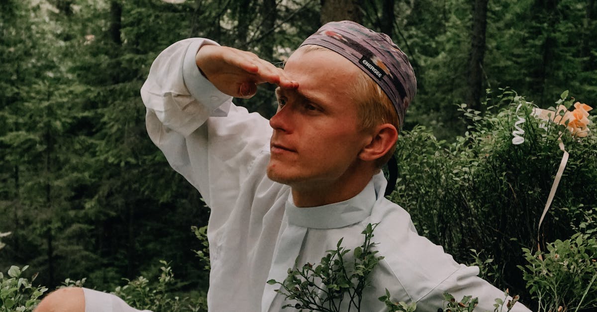 A man in adventurous pose crouches in a lush forest, searching the horizon.