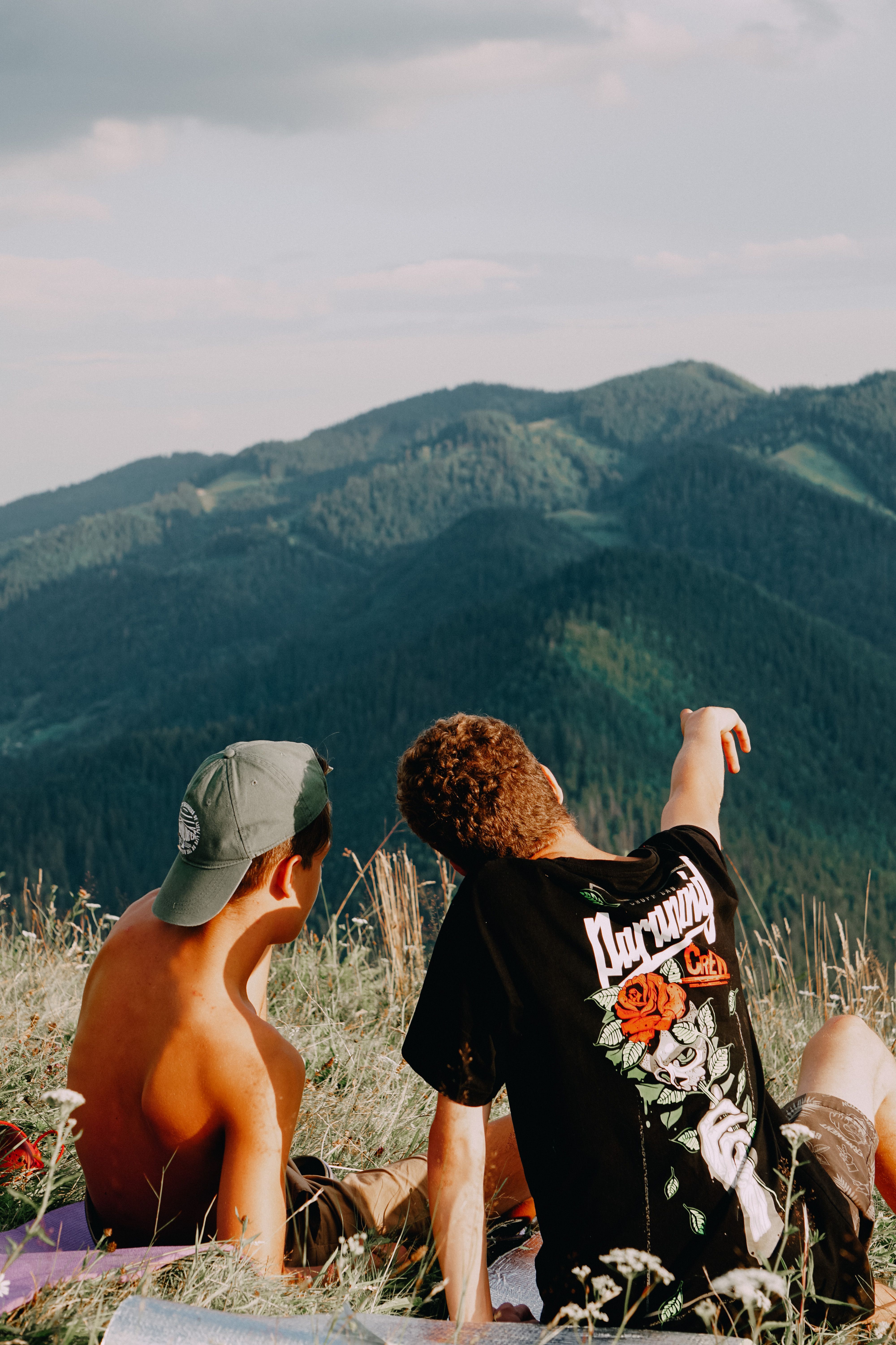 Two men sitting on a hillside, enjoying a scenic mountain view under a clear sky.