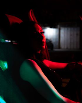 A dramatic and mysterious portrait of a woman sitting in a car at night with colorful lighting.