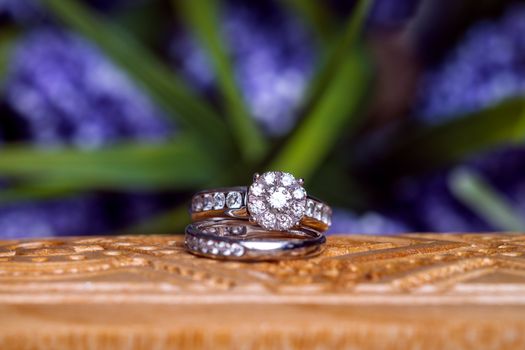 Wycena biżuterii z brylantami: Jak ocenić kamienie szlachetne w 2026 roku? 1 Close-up of diamond wedding rings on carved wood against a blurred floral background.