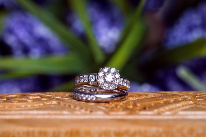 Close-up of diamond wedding rings on carved wood against a blurred floral background.