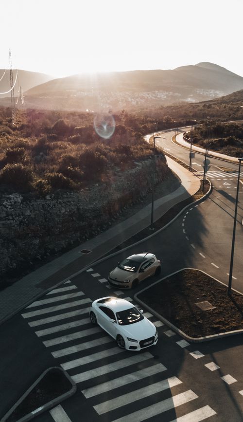 Free Aerial view of a scenic road in Tivat, Montenegro during a stunning sunset, showcasing two cars and a winding path. Stock Photo