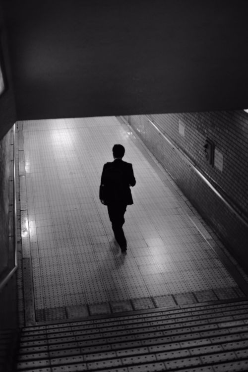 Free A solitary man walks through a tunnel, captured in black and white for dramatic effect. Stock Photo