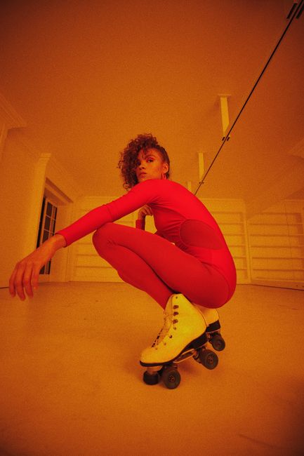 Woman in bright red outfit crouching on roller skates indoors, exuding energy.