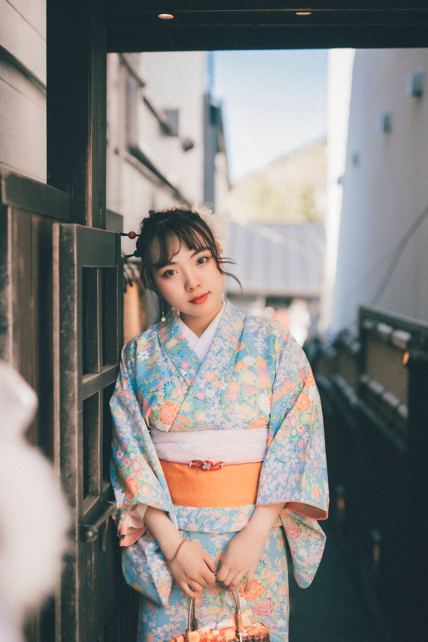 Portrait of a Japanese woman in kimono standing at a traditional doorway.