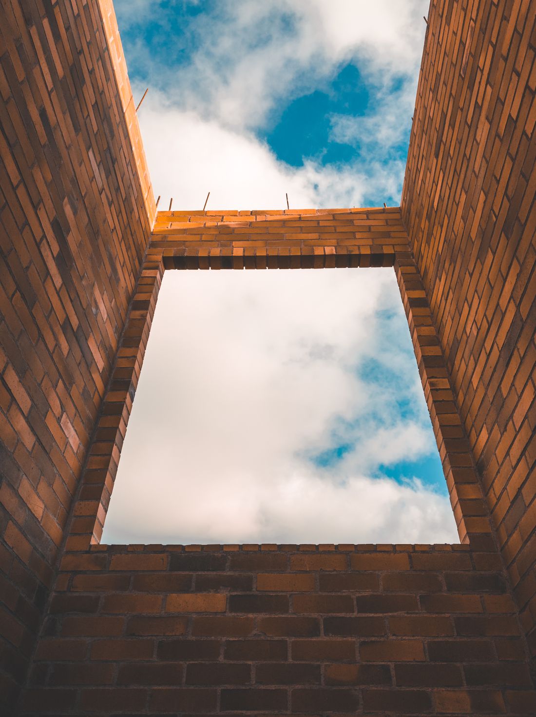 Muros de ladrillo sin terminar en una construcción, con aberturas y cielo visible. Fotografía ilustrativa de mampostería.