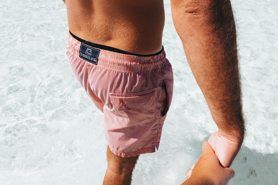 A man in swimwear holds hands while strolling in clear tropical waters.