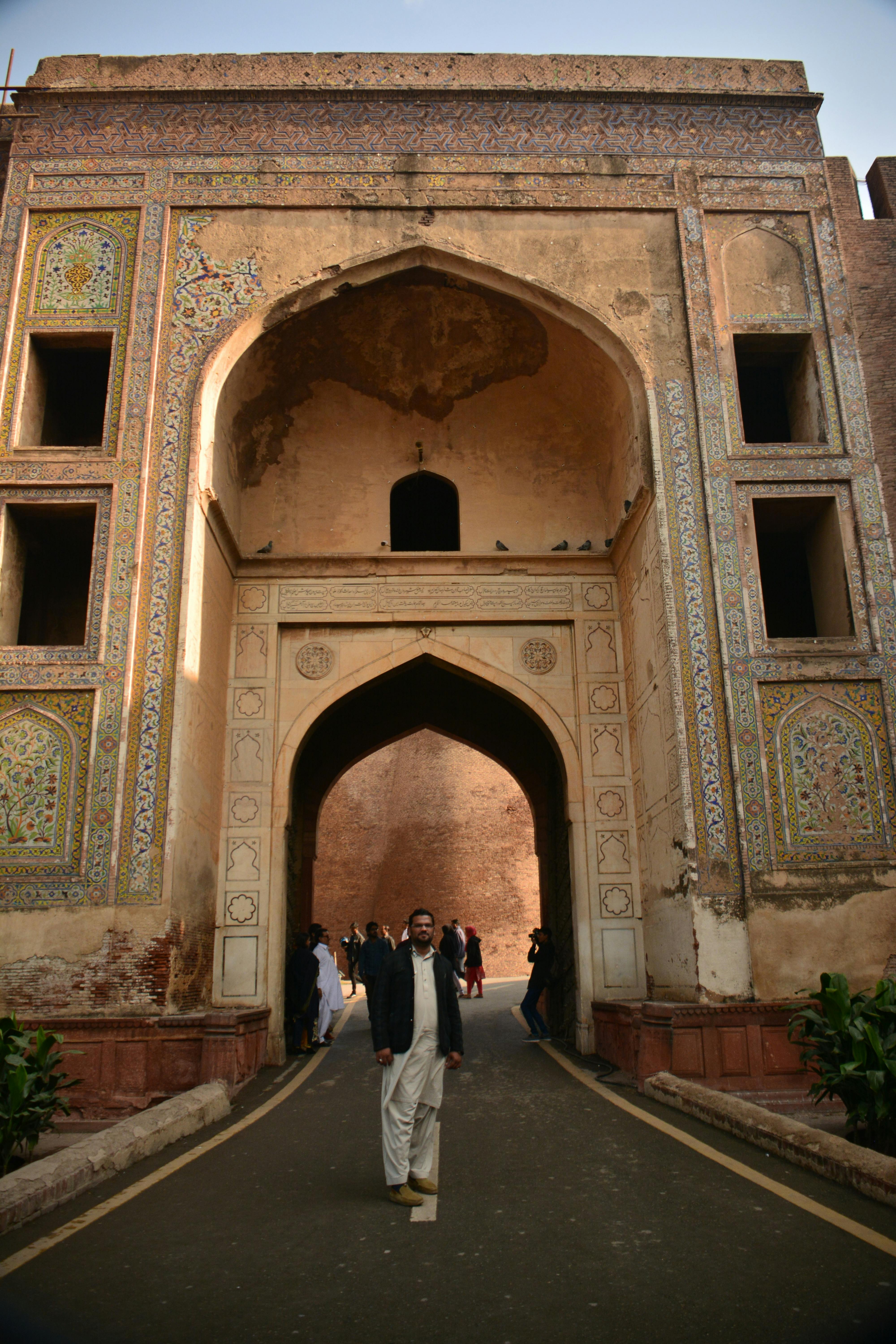 A man walks through a historic Mughal-style archway in Lahore, showcasing intricate architecture and cultural heritage.