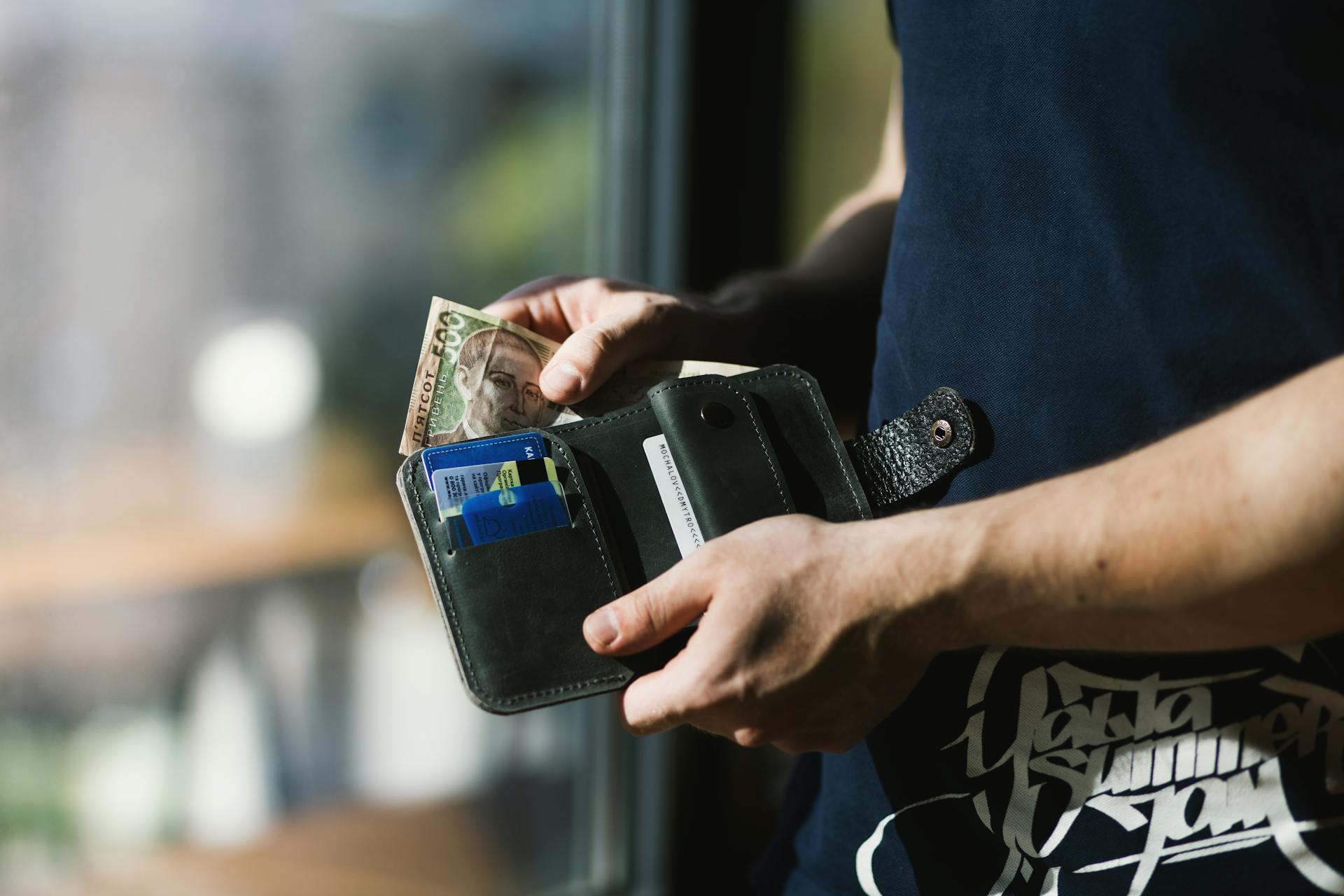 Close-up of a man holding a wallet with cash and credit cards, indoors.