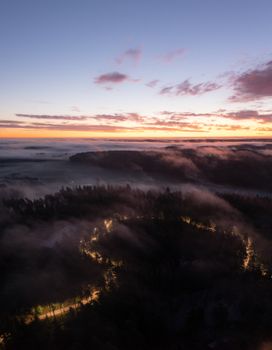 Aerial view of a foggy forest and winding road at sunset in Lieto, Finland.