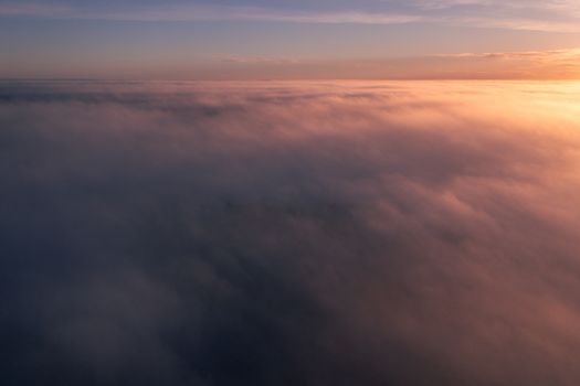 A breathtaking aerial view of clouds illuminated by the warm hues of a sunset, capturing tranquility.