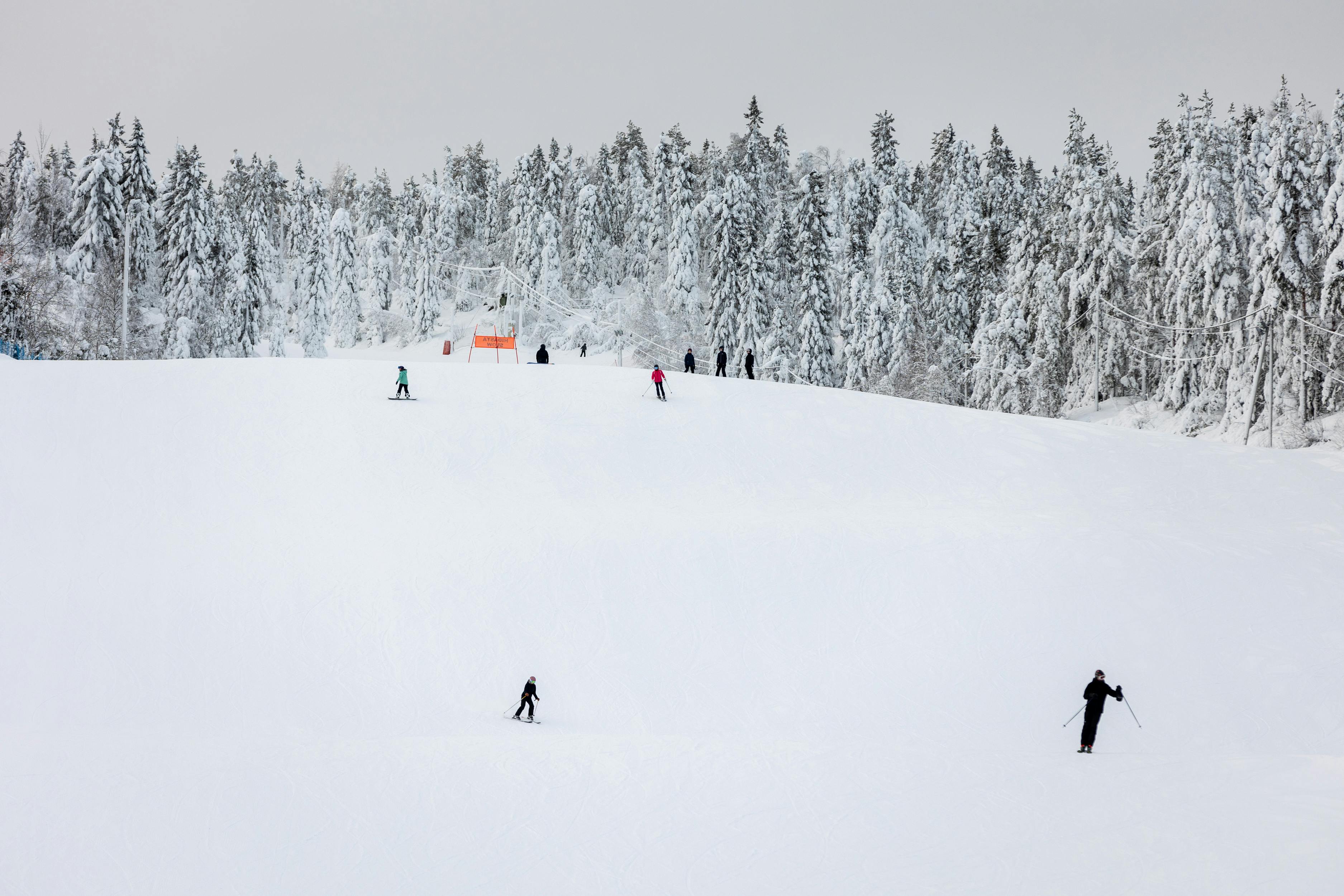 Prescription Goggle Inserts - Skiers gliding down the snowy slopes of Vuokatti, Finland, surrounded by a winter forest.