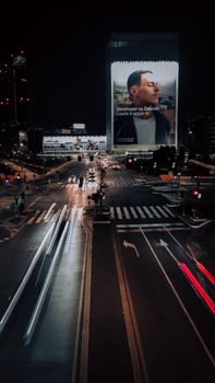 Long exposure of traffic and illuminated billboard in Milan at night.