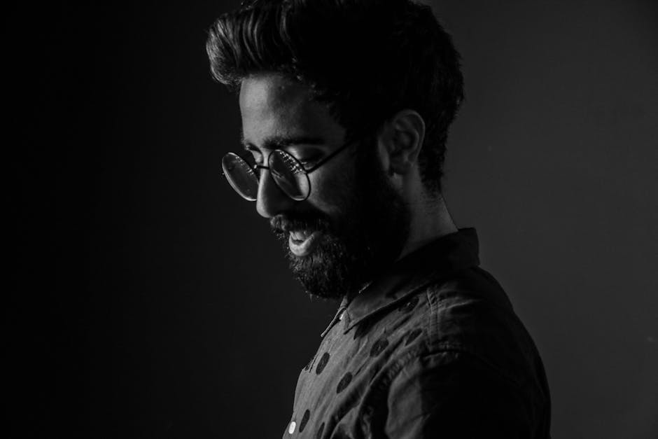Black and white portrait of a fashionable bearded man with glasses, in side profile.