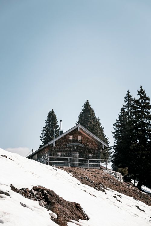 Free Snow-covered cabin in Tegernsee with a clear blue sky and green pines, capturing a serene winter scene. Stock Photo