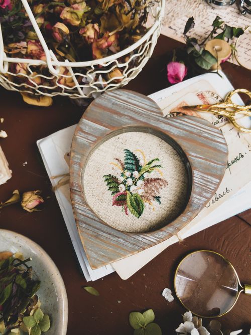 Free A heart-shaped wooden frame featuring delicate embroidered flowers in a flat lay setting. Stock Photo
