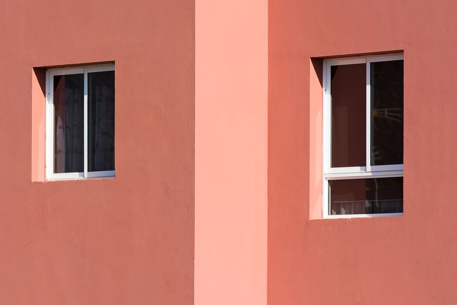 Closeup of a pink building facade featuring two white-framed windows.