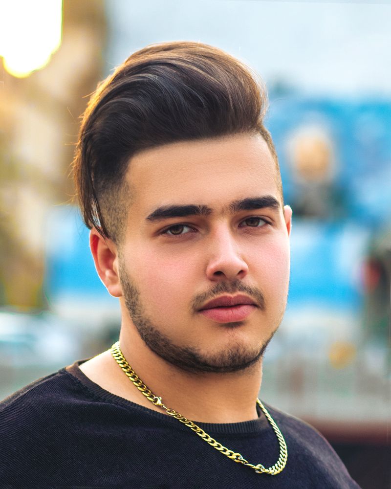 Close-up portrait of a young man with a stylish haircut and gold necklace outdoors.