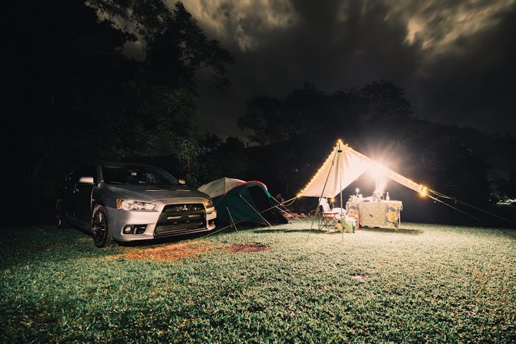 A Silver Car And Tents On A Camping Site At Night