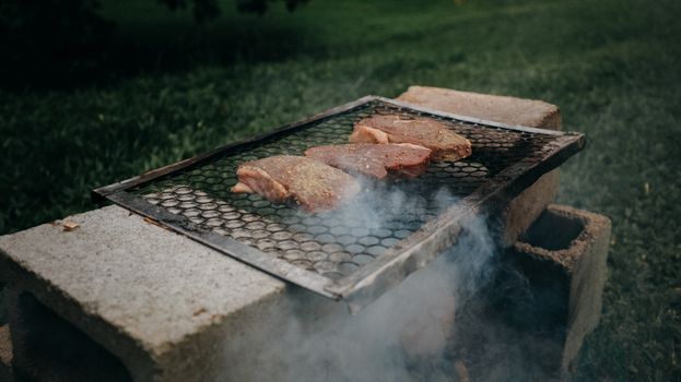 Juicy meat chops grilling on a smoky outdoor barbecue on a summer day.