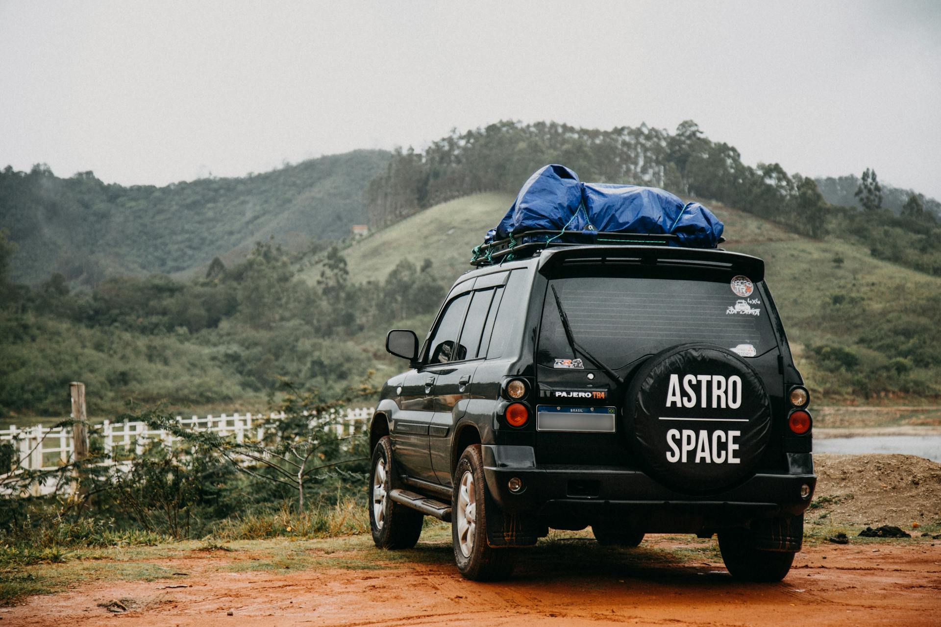 Black SUV with roof rack in front of lush hills and dirt path.
