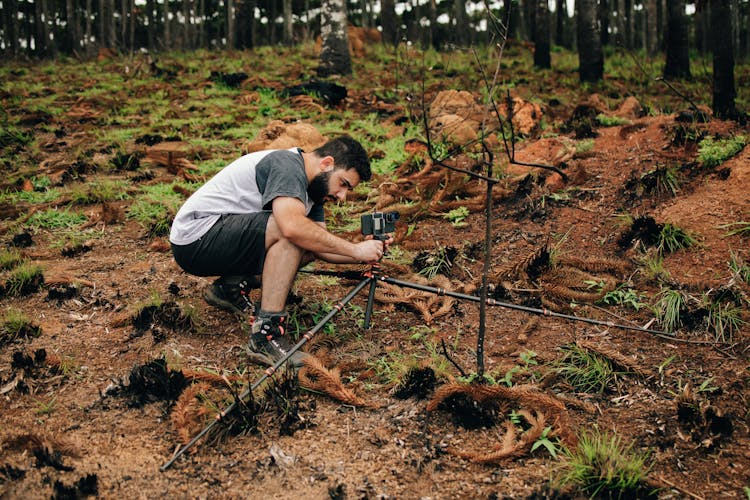 Man Installing Camera On Ground In Woodland