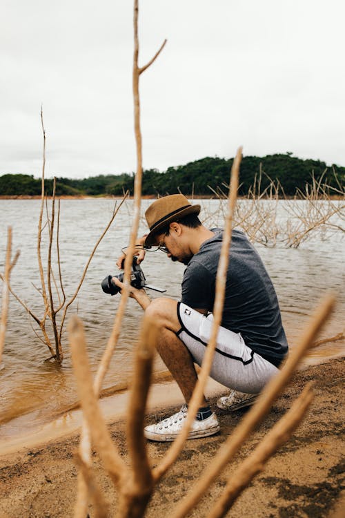Man Crouching on Lake Shore and Taking Photo 