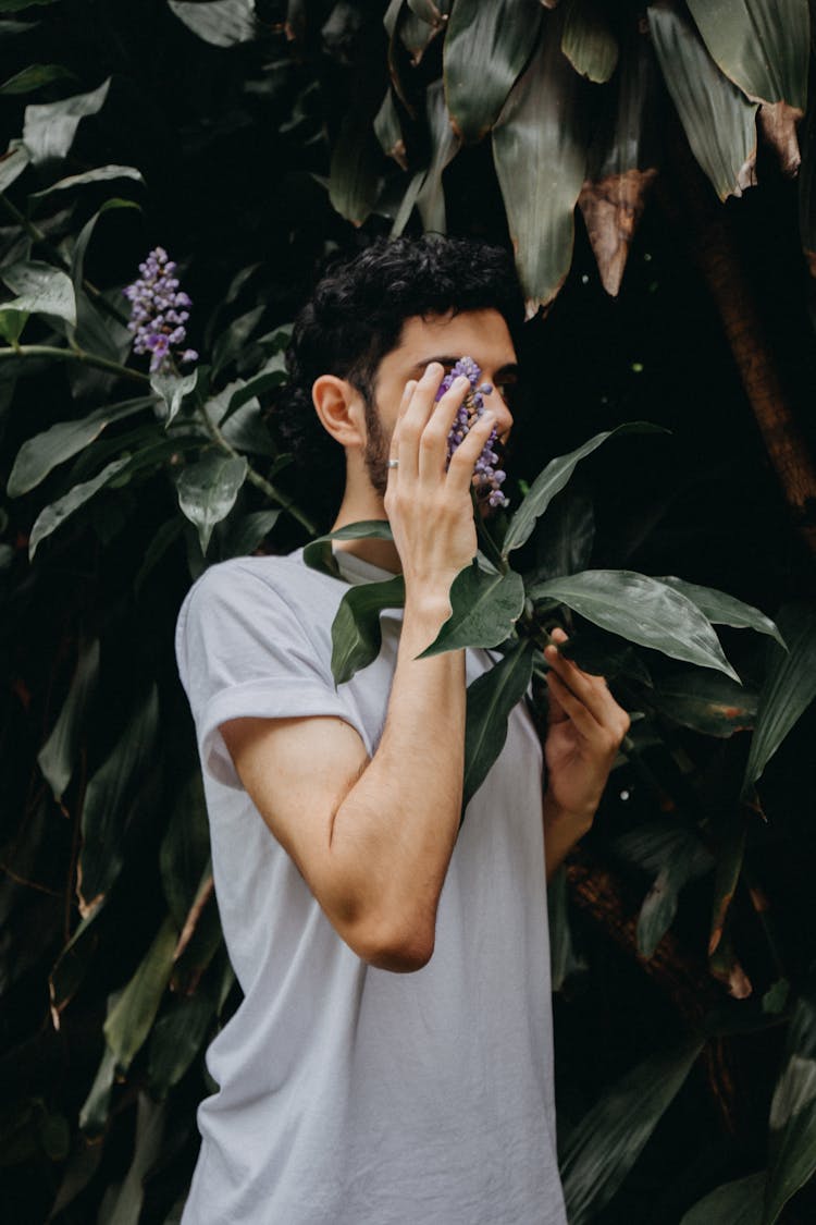 Man Standing By Shrub And Covering Face With Hand