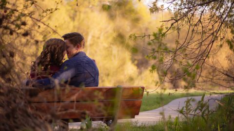 A couple enjoying a cozy moment on a park bench surrounded by nature.