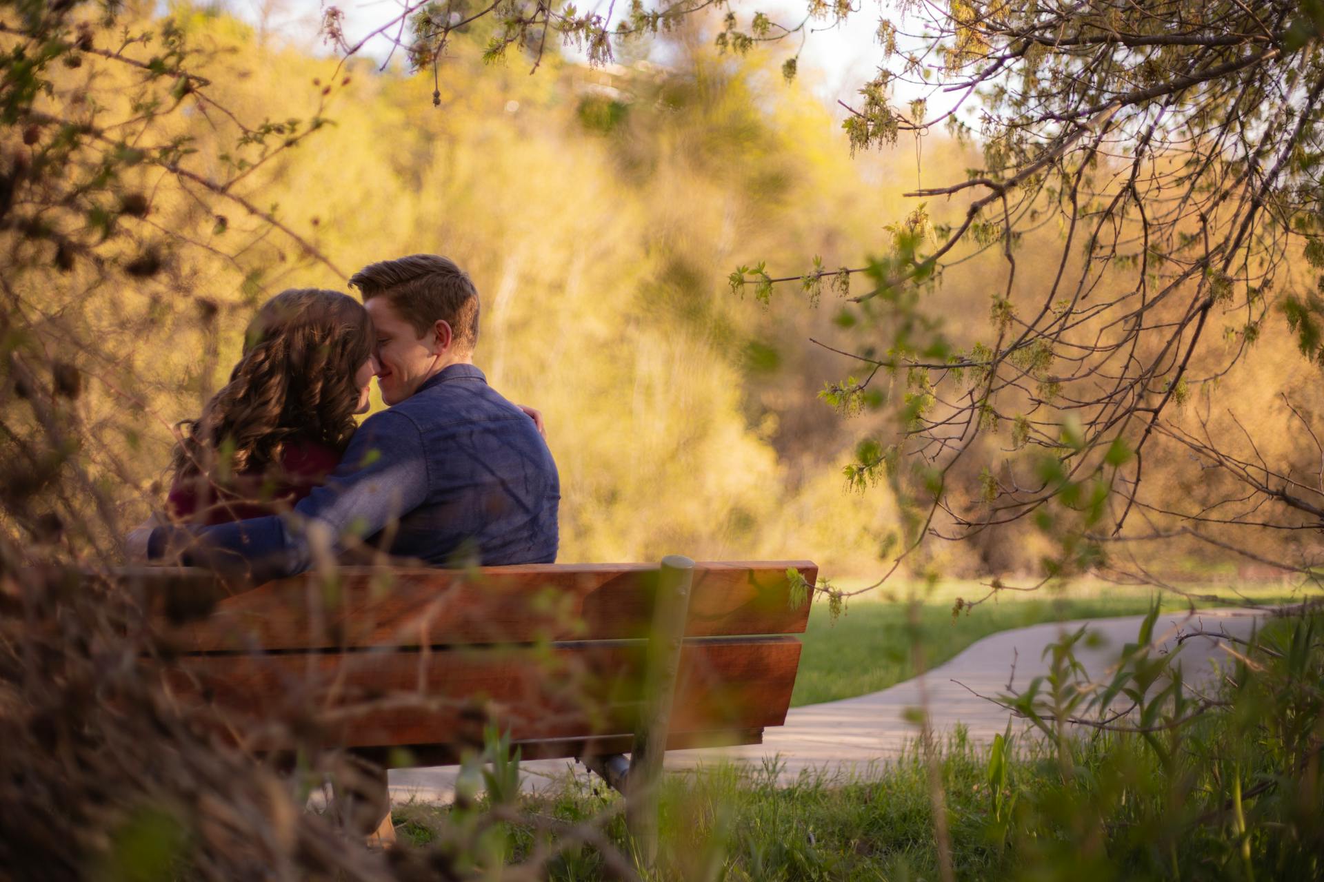 A couple enjoying a cozy moment on a park bench surrounded by nature.