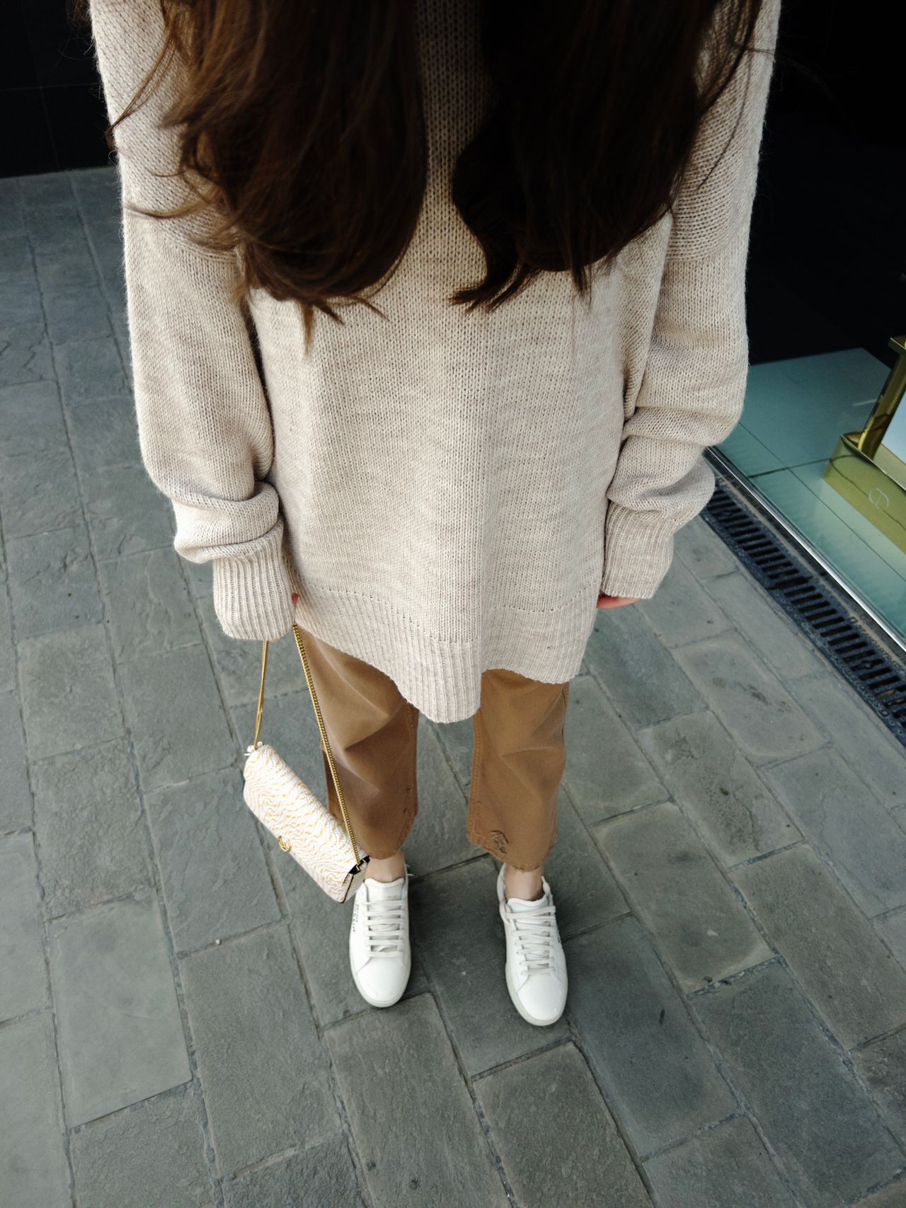 Woman in an oversized cream knit sweater, tan pants and white sneakers