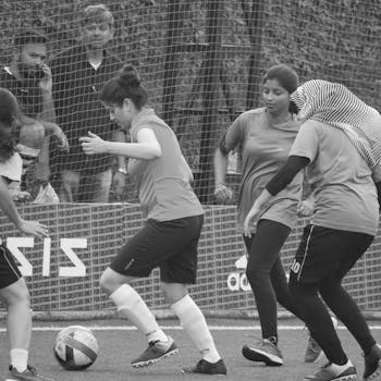 Dynamic grayscale photo of women playing soccer with intensity and focus on teamwork.