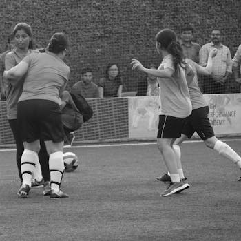Dynamic black and white image of women playing soccer outdoors, emphasizing teamwork and athleticism.