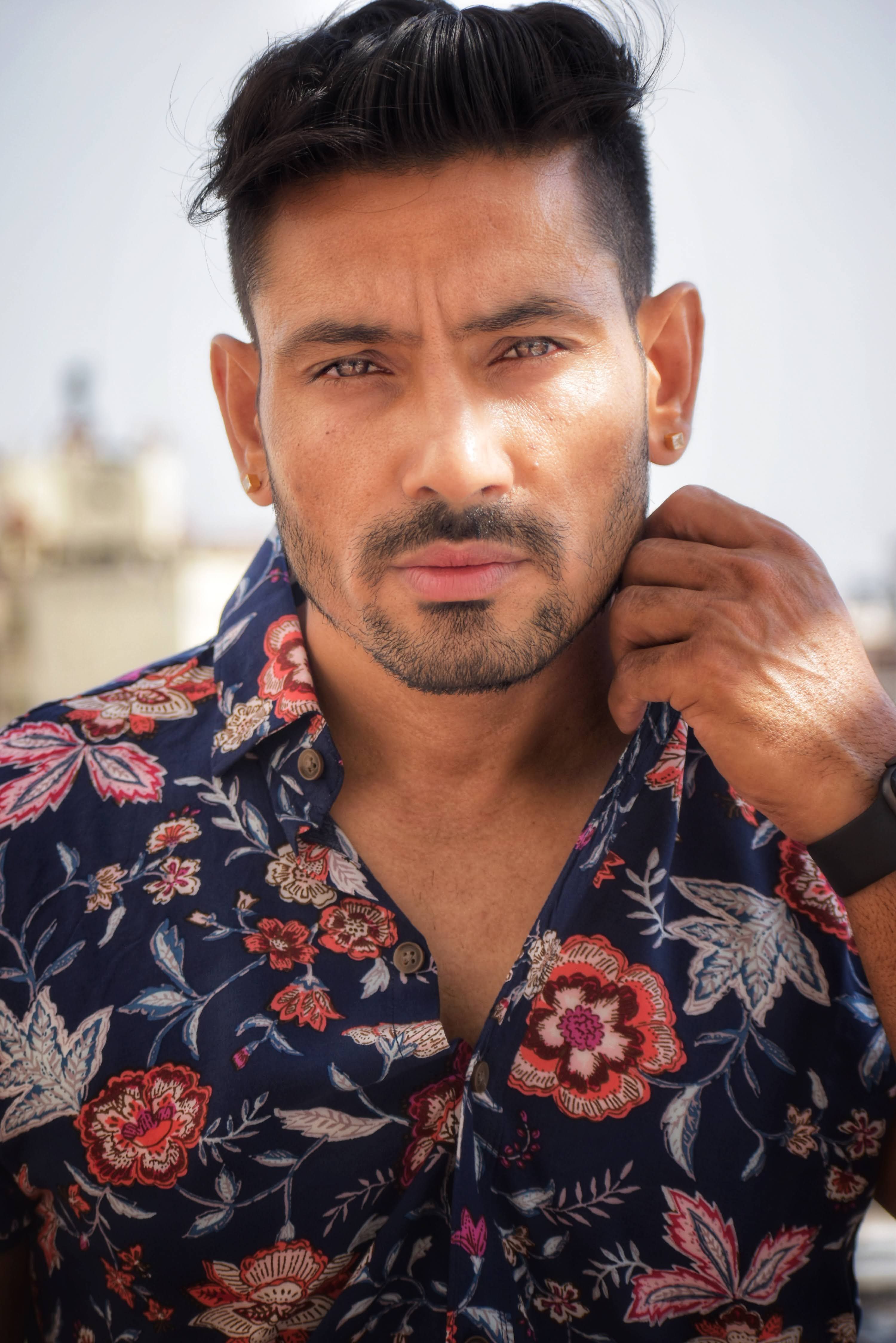 Close-up portrait of a man in a floral shirt, outdoors on a sunny day.