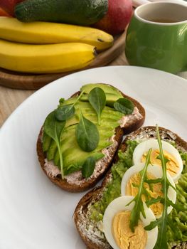 Delicious breakfast with avocado toasts, boiled eggs, and fresh fruits.