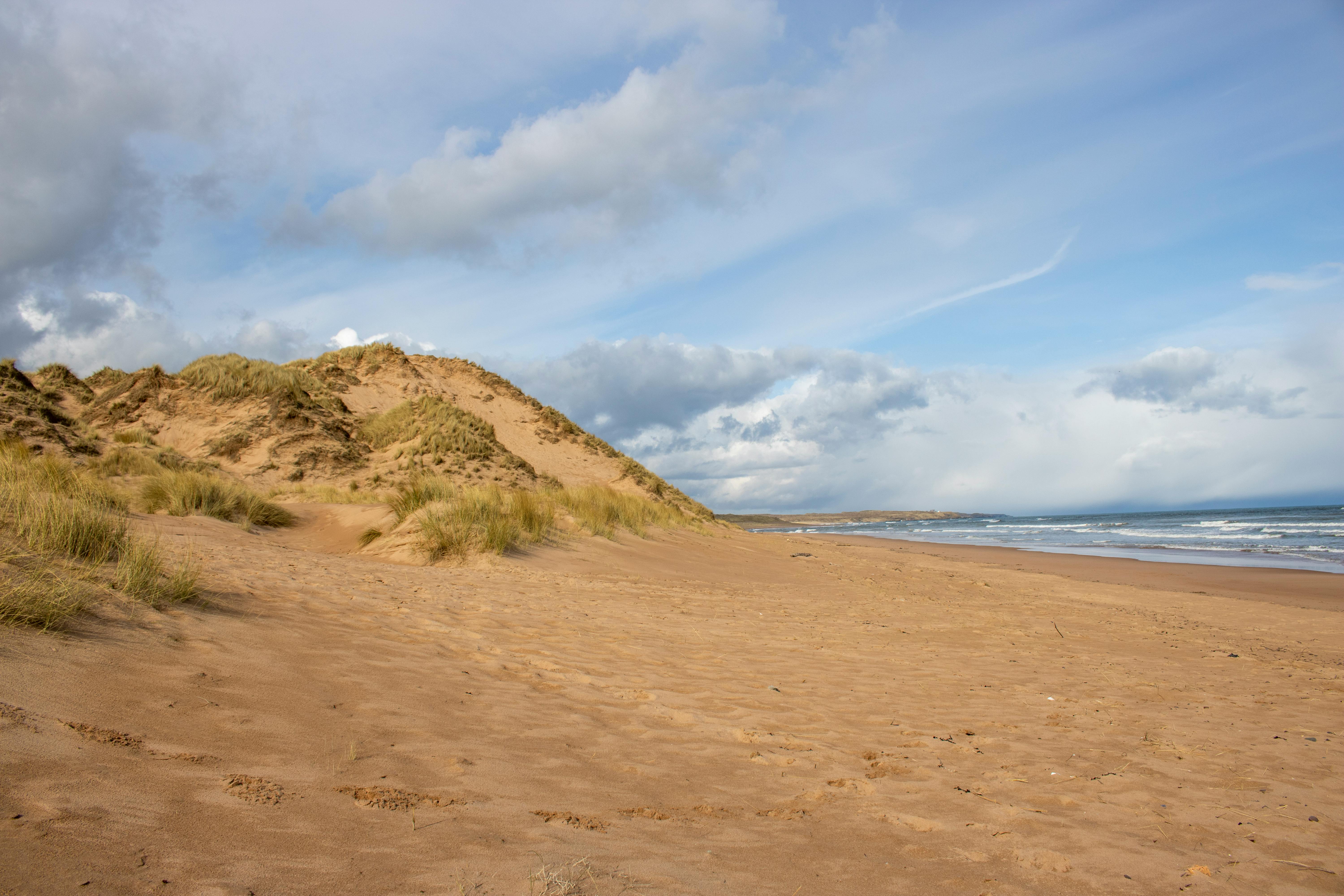 Scenic view of Newburgh's sandy beach with rolling dunes under a partly cloudy sky.