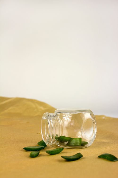 Free A glass jar tipped over on sand with fresh aloe vera slices spilling out, creating a natural and minimalist scene. Stock Photo