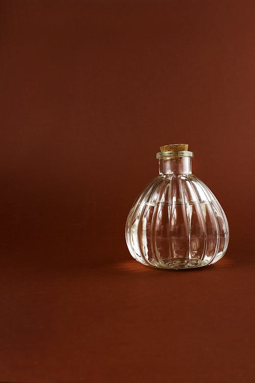 Close-up Photo of Clear Glass Bottle on a Maroon Background 