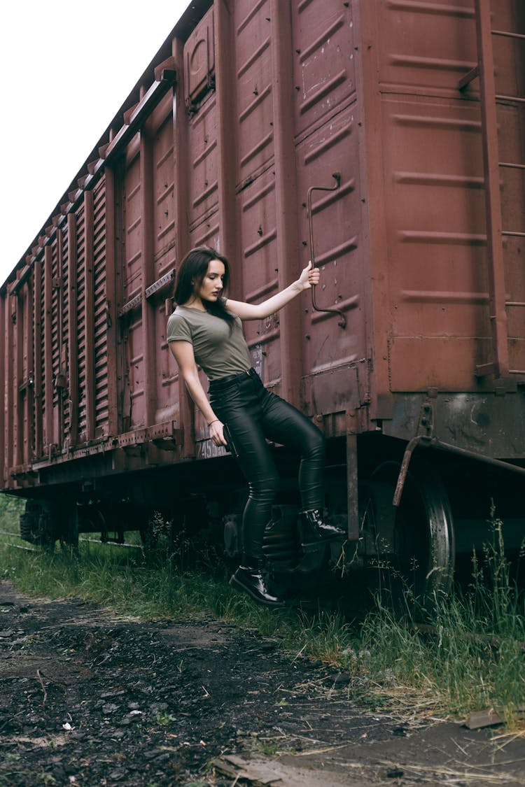 A Woman Hanging On A Cargo Train While Holding A Handgun